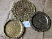 Photo of three round brass trays grouped together on a cloth background, showing various engraved patterns and sizes.