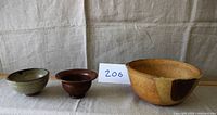 Photo showing side view of three handcrafted pottery bowls in different colors and sizes, arranged on a neutral fabric.