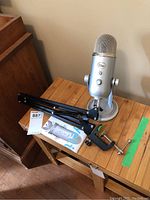 Blue Yeti microphone on silver base next to detached black metal desktop arm with clamp on wooden table.