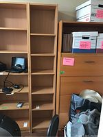 Full height of the pressboard bookcase in a light wood finish beside a chest of drawers and miscellaneous items.