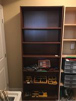 Full view of the tall bookcase showing 5 shelves, mostly empty except the bottom shelf containing various items not included in the lot.