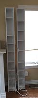 Two tall narrow white wooden shelves against a wall with multiple adjustable shelf compartments.