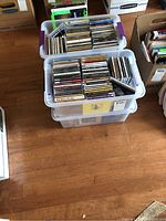 Photo of two stacked clear plastic storage bins with numerous CDs organized inside, showing spines and some album covers