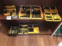 Overall view of multiple DeWalt drill bit cases, screwdriver, and accessories on a wooden shelf.