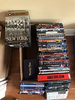 Overall view of DVDs in a cardboard box, showing PBS DVD Gold New York documentary, Family Ties series box, and West Side Story in a red case along with various DVDs stacked.