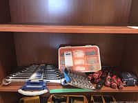 Overall view of all items on shelf showing combination wrench set, assorted screwdrivers, tape measure, socket set and fastener box