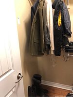 Full view of hanging jackets and blazers with rubber boots below on floor.