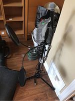 Full microphone setup with Shure SM58 mic mounted on black tripod Ultimate Support stand with two attached round pop filters and attached cable. Setup leaning against wall on wooden floor.