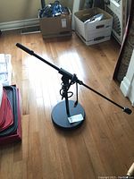 Full view of the K&M black adjustable tabletop microphone stand with articulating arm and cable attached, placed on a hardwood floor.