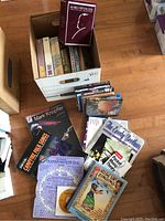 Photo showing a white box filled with CD cases and a red Alfred Hitchcock DVD box on top. Multiple songbooks and CDs are laid out around the box, titles include Mark Knopfler, Carole Brothers, and 'Rise Up Singing'.