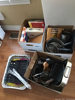 Box of cookbooks, metal pots and pans, and a box with kitchen tools and knives.