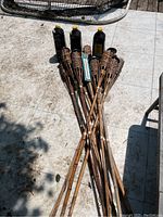 12 bamboo tiki torches laid on a stone or tiled floor with three full bottles of tiki torch fuel placed behind them.