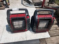 Two Mr. Heater BIG Buddy space heaters side by side on a tiled surface showing front and top views with carrying handles.