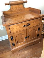 Front view of wooden wash stand showing top, drawer with black handle, and lower cupboard with two doors featuring black hinges and knobs.