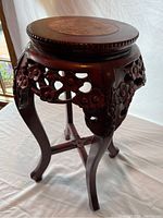 Full view of round wooden side table with carved floral apron and four curved legs