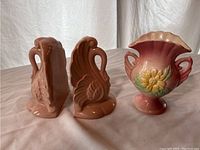 Two ceramic pink swan bookends and one pink floral vase showing overall lot contents.