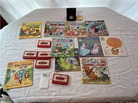 Image showing nine Walt Disney children's books and nine matching red cassette tapes, plus a limited edition coin in black velvet display box.