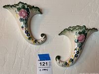 Pair of ceramic wall pockets on wall, showing matching floral painted decoration and green accents.