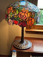 Full view of the stained glass table lamp showing floral shade and metal base on wooden table.