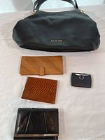 Full lot including Michael Kors black leather purse and four assorted wallets arranged on a cloth surface, showing purse size and wallet variety.