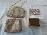 Four mini purses including a large beaded purse with handle, a floral patterned rectangular purse, a square beaded purse, and a small gold mesh purse arranged on a white cloth.