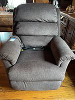 Front view of dark brown fabric motorized easy chair showing padded backrest, armrests, seat, and remote control with buttons on armrest.