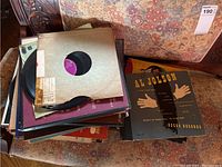 Overview of vinyl records stacked on a patterned chair, showing some records in paper/ cardboard sleeves and an Al Jolson record visible