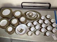 Full array of china pieces on table showing different types of plates, cups, saucers, and serving pieces with distinct gold and green detailed rim pattern.