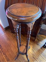 Full view of the tall round wooden side table showing turned legs and tripod base on a hardwood floor.