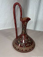 Side view of vintage Biagioli Gubbio ceramic pitcher with detailed floral and ribbon design on red background.