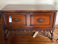Front view of wooden cedar chest with carved details and large metal handles on front panels.