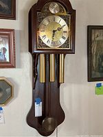 Full view of the wooden wall clock including pendulum, weights, and dial.