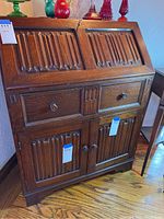 Front view of wood secretary desk showing embossed carved panels on drop front and front cabinet doors plus drawer pulls.