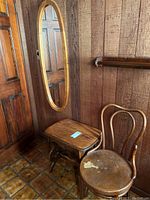 Side table, chair, and oval mirror arranged in corner near door with wood panel walls and tile floor.