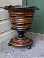 Full view of turned mahogany wine bucket showing body shape, black accent rings, pedestal base and bun feet