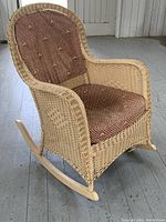 Front side view of antique wicker rocking chair showing fabric upholstery and rocker base.