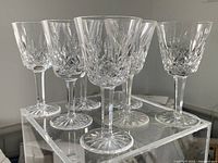 Seven crystal wine glasses arranged on clear acrylic riser