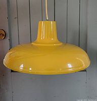 Yellow Mid-Century Modern style hanging pendant light about 16 inches in diameter with a long cord, glossy finish, shown against a gray wooden background.