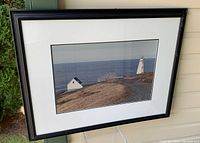 Full view of framed photograph showing the lighthouse and surrounding coastal area with clear sky and sea in the background.