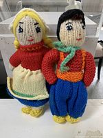 Photo showing a pair of vintage knitted folk art dolls, one female with yellow braids and one male with black hair.