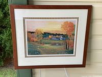 Framed gallery art print showing autumn landscape in wooden frame hung on wall.