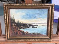 Frontal image of the signed landscape oil painting depicting coastal rocks, water, and trees in an ornate frame.