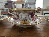 Close-up of Royal Albert white and red rose pattern cup on matching saucer with gold interior and trim