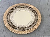 Top down view of the circular vintage rattan-framed mirror lying flat on a wooden floor, showing its detailed weave pattern in natural and dark rattan tones.