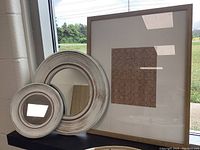 Framed art and two round white framed mirrors displayed together.