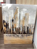 Front view of the large stretched canvas painting depicting an abstract cityscape with tall buildings in subtle earth tones.