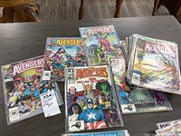 Photo showing a wide view of the comic book lot laid out on a table, including visible covers of several Avenger comic book issues in protective bags.