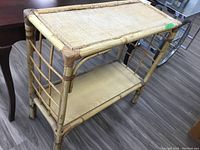 Front and side view of bamboo table showing woven top, wooden shelf, and structural frame of bamboo rods with bindings, placed on wood flooring.