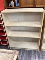 Full front view of the light-colored laminate bookcase showing three shelves and overall condition.