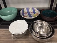 Nine serving bowls and dishes, four mixing bowls, and one lidded Pampered Chef measuring jug arranged side by side on a shelf.